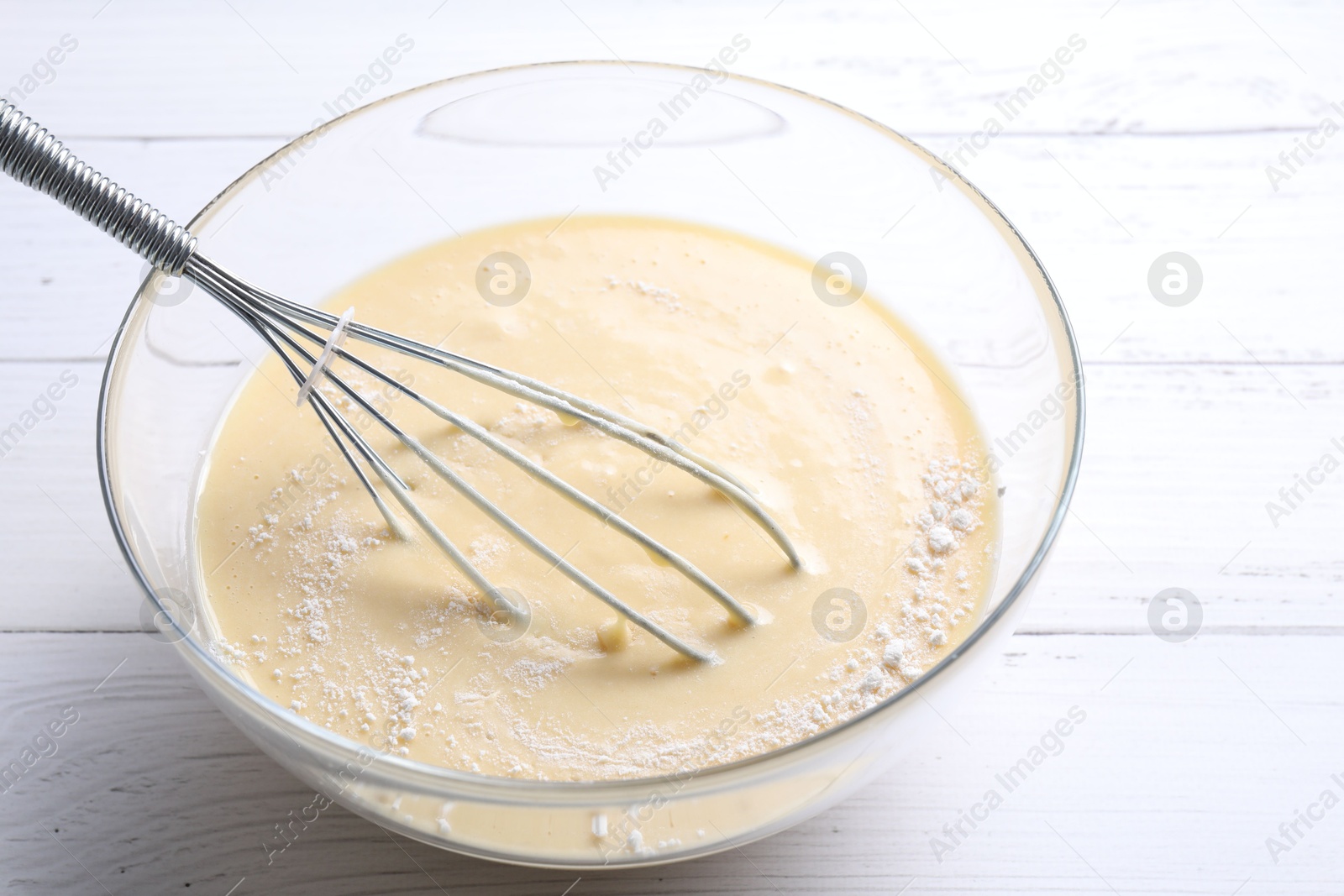 Photo of Whisk and bowl of dough on white wooden table, closeup