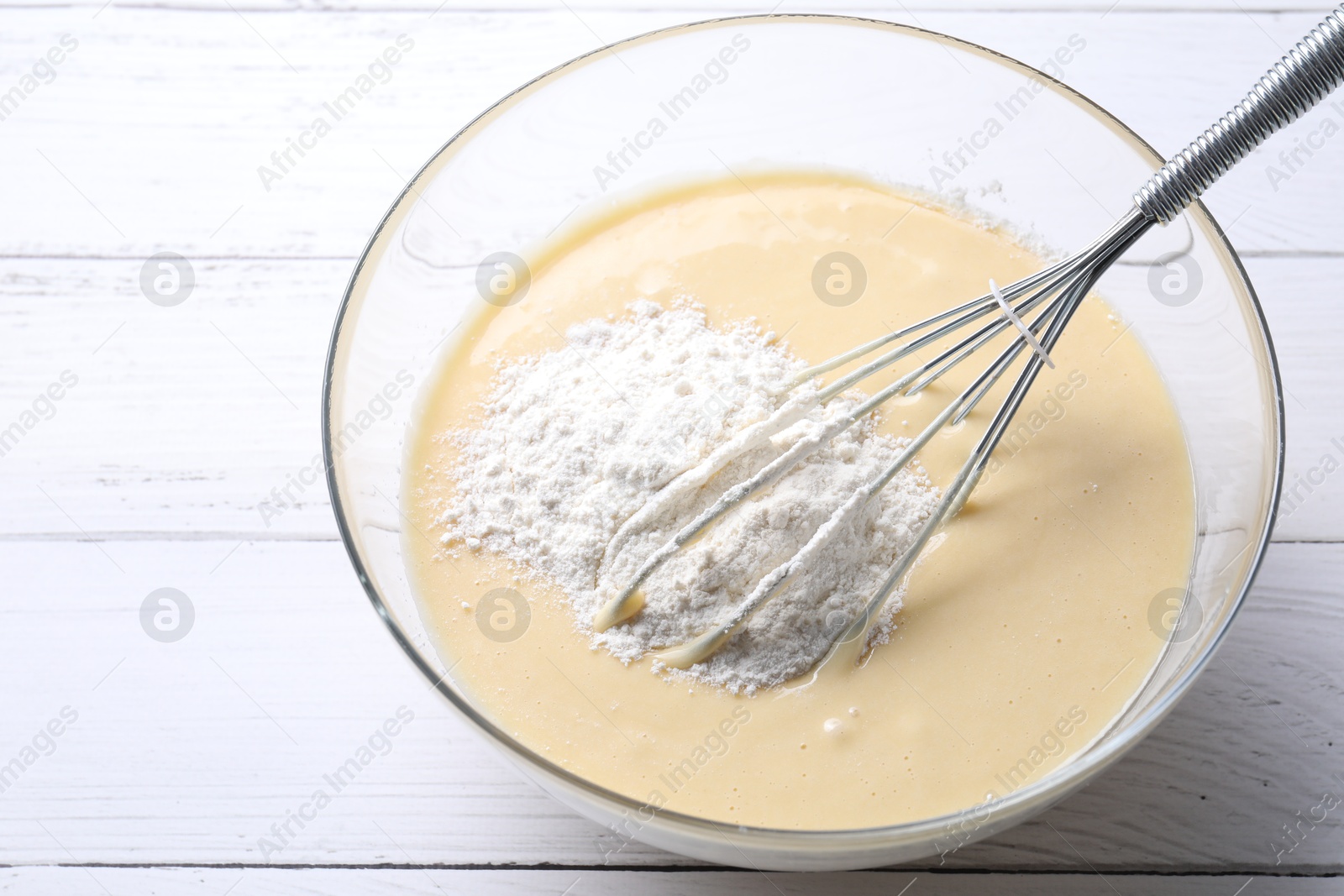 Photo of Whisk and bowl of dough on white wooden table, above view