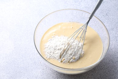 Photo of Whisk and bowl of dough on grey table, closeup. Space for text