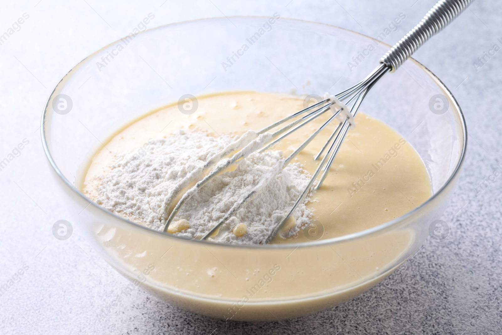 Photo of Whisk and bowl of dough on grey table, closeup