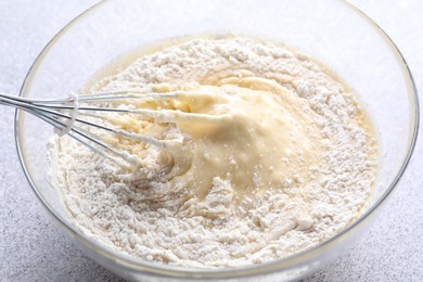 Photo of Whisk and bowl of dough on grey table, closeup