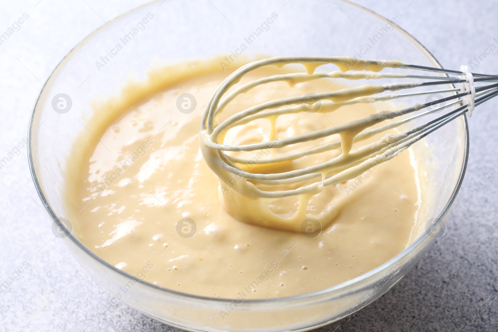 Photo of Whisk and bowl of dough on grey table, closeup