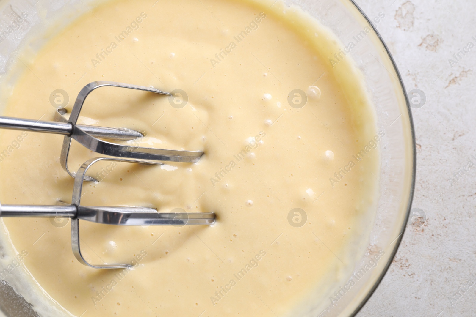 Photo of Making dough in bowl with hand mixer at grey table, top view