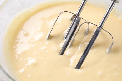 Photo of Making dough in bowl with hand mixer, closeup