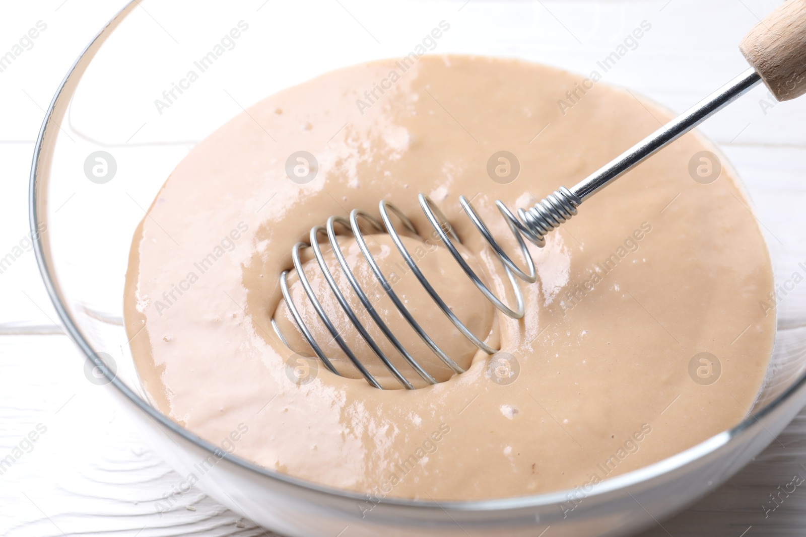 Photo of Whisk and bowl of dough on white wooden table, closeup