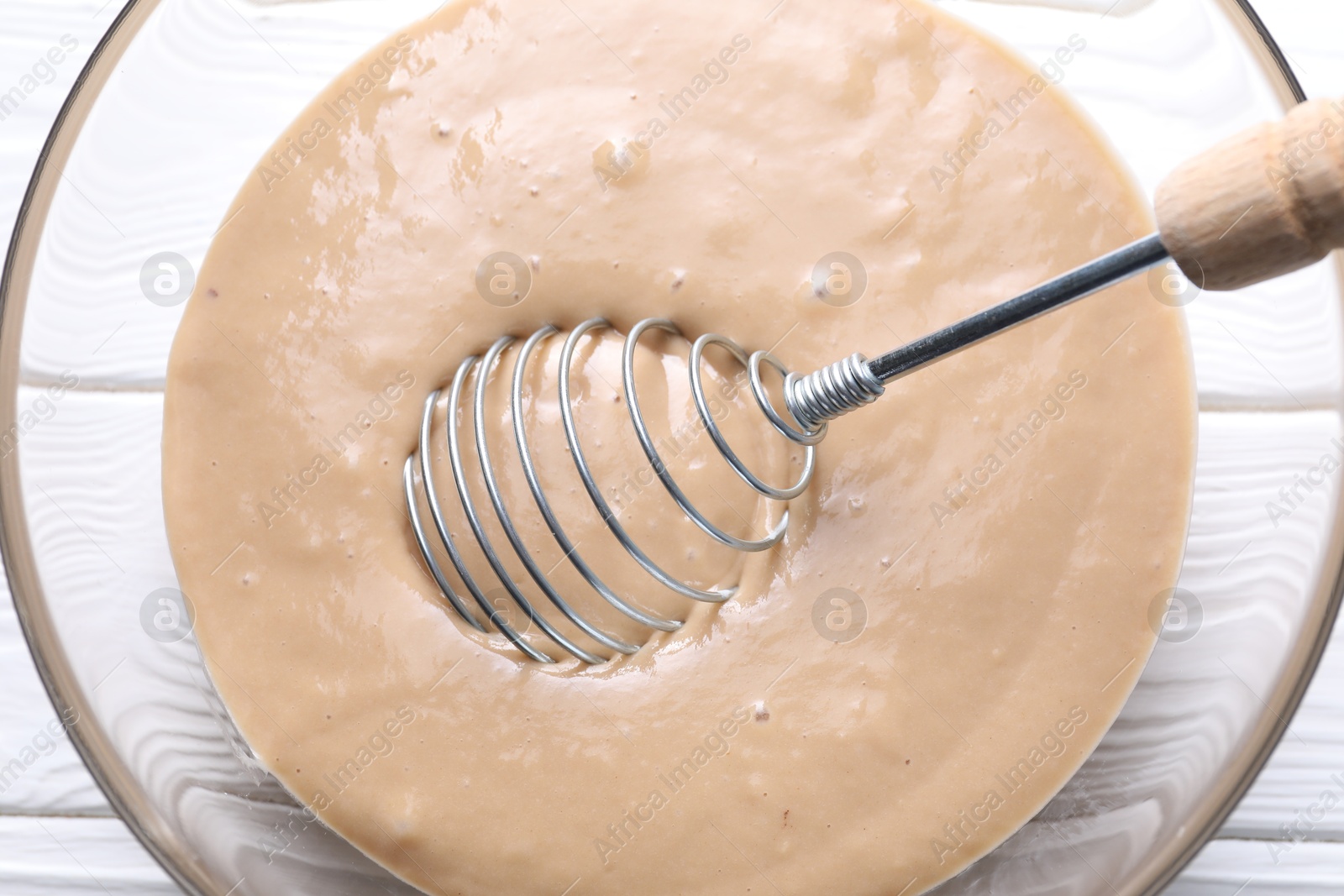 Photo of Whisk and bowl of dough on white wooden table, top view