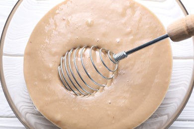 Photo of Whisk and bowl of dough on white wooden table, top view