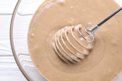 Photo of Whisk and bowl of dough on white wooden table, top view