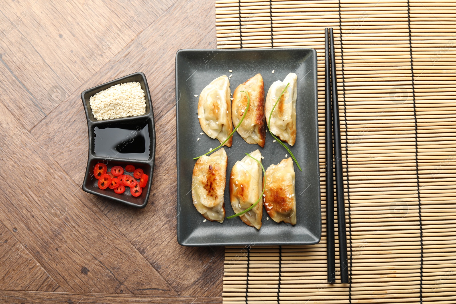 Photo of Delicious fried gyoza dumplings with sesame seeds served on wooden table, flat lay