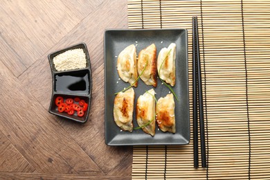 Delicious fried gyoza dumplings with sesame seeds served on wooden table, flat lay