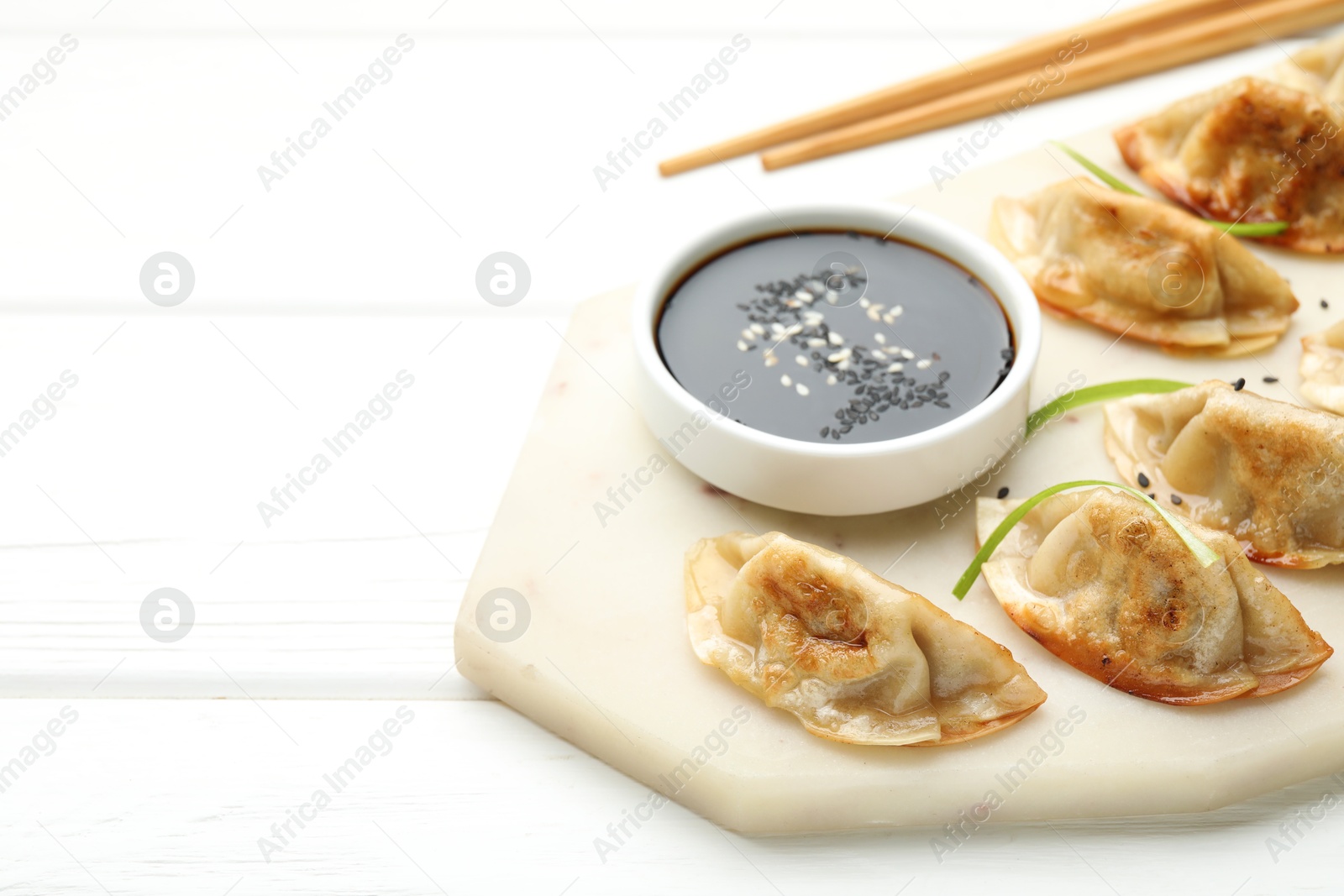 Photo of Delicious fried gyoza dumplings with sesame seeds served on white wooden table, closeup. Space for text