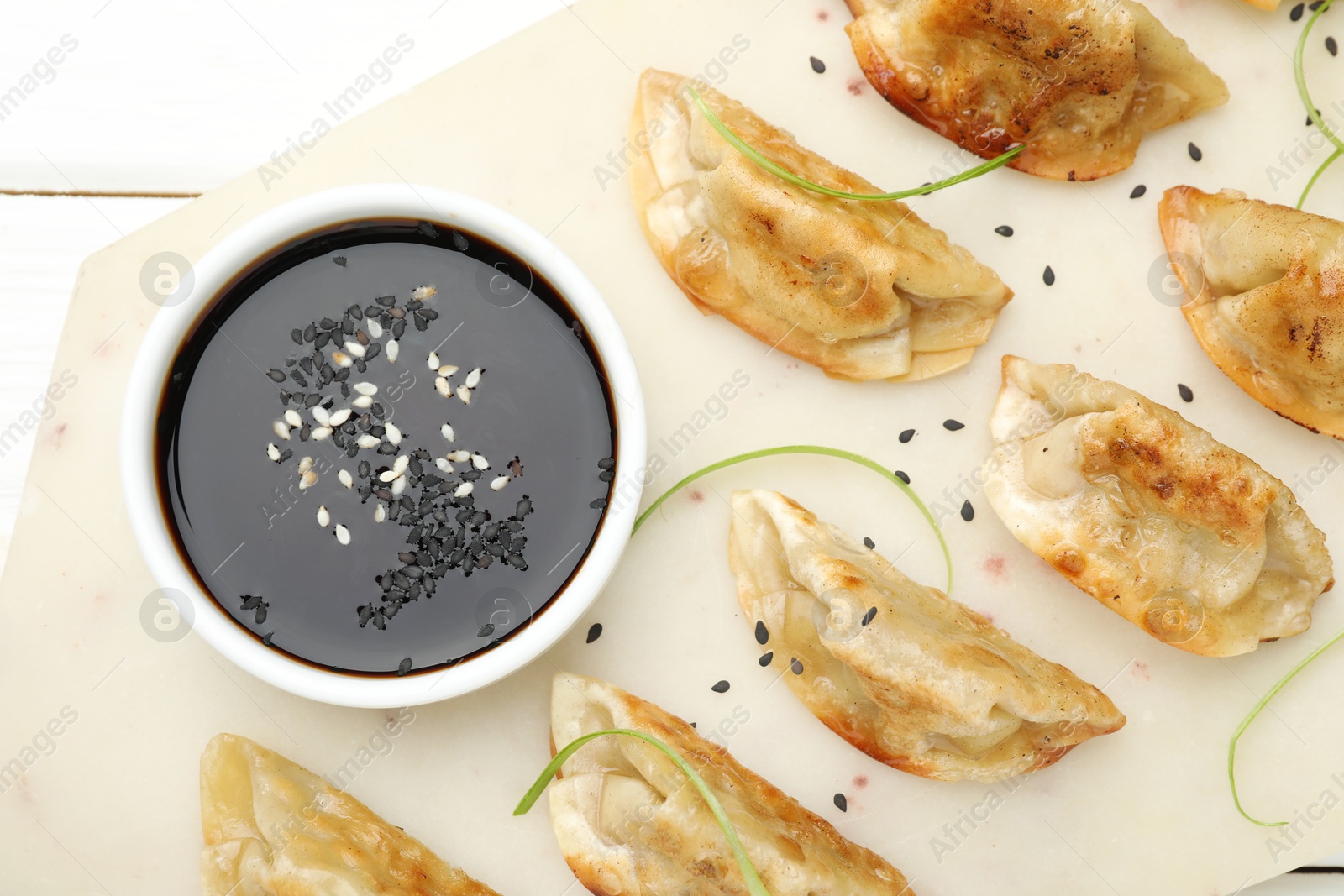 Photo of Delicious fried gyoza dumplings with sesame seeds served on white table, top view