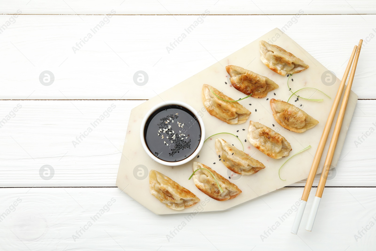 Photo of Delicious fried gyoza dumplings with sesame seeds served on white wooden table, top view. Space for text