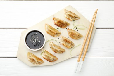 Delicious fried gyoza dumplings with sesame seeds served on white wooden table, top view