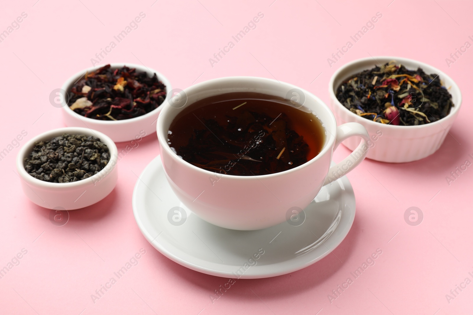 Photo of Aromatic tea and dried leaves on light pink background, closeup