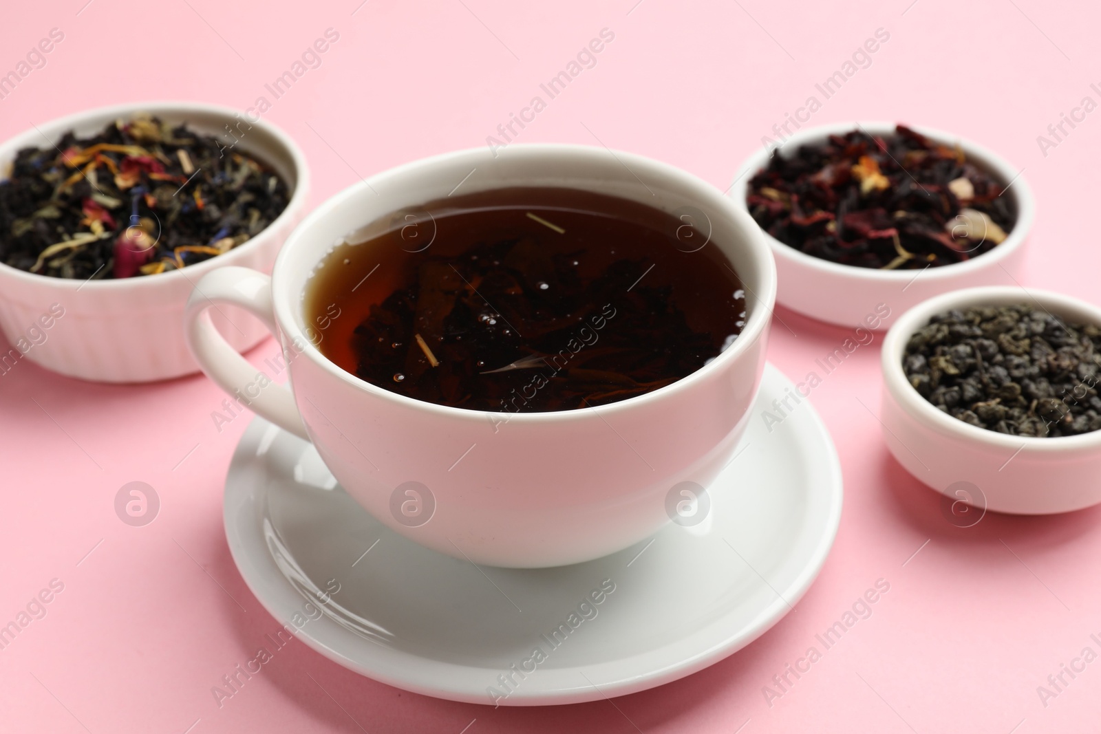 Photo of Aromatic tea and dried leaves on light pink background, closeup