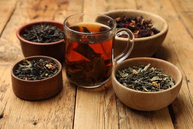 Photo of Aromatic tea and dried leaves on wooden table, closeup