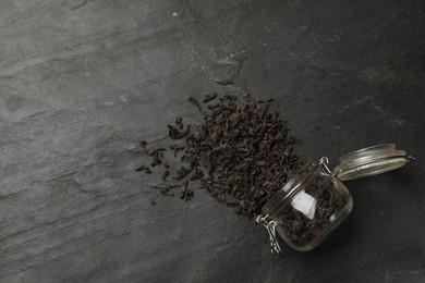 Photo of Dried tea leaves and jar on black table, top view. Space for text