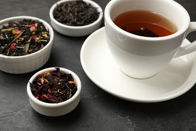 Photo of Aromatic tea and dried leaves on black table, closeup