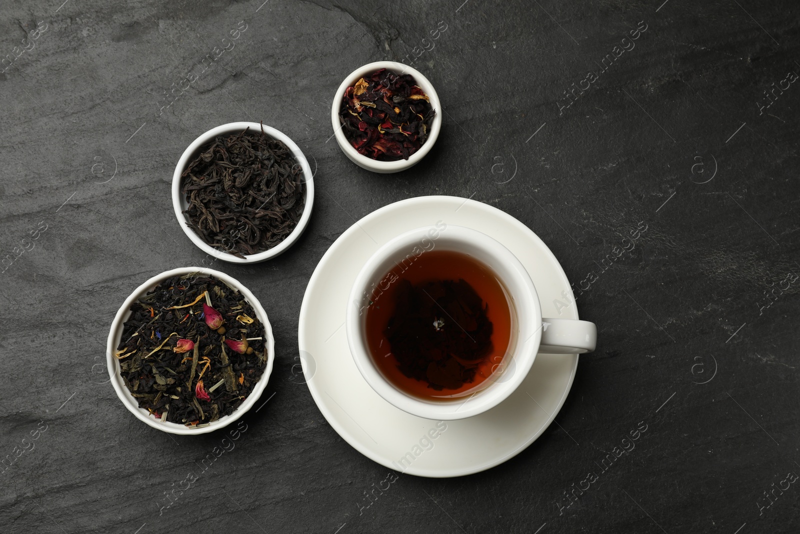 Photo of Aromatic tea and dried leaves on black table, flat lay