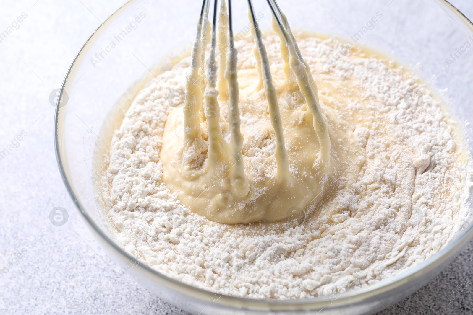 Photo of Whisk and bowl of dough on grey table, closeup