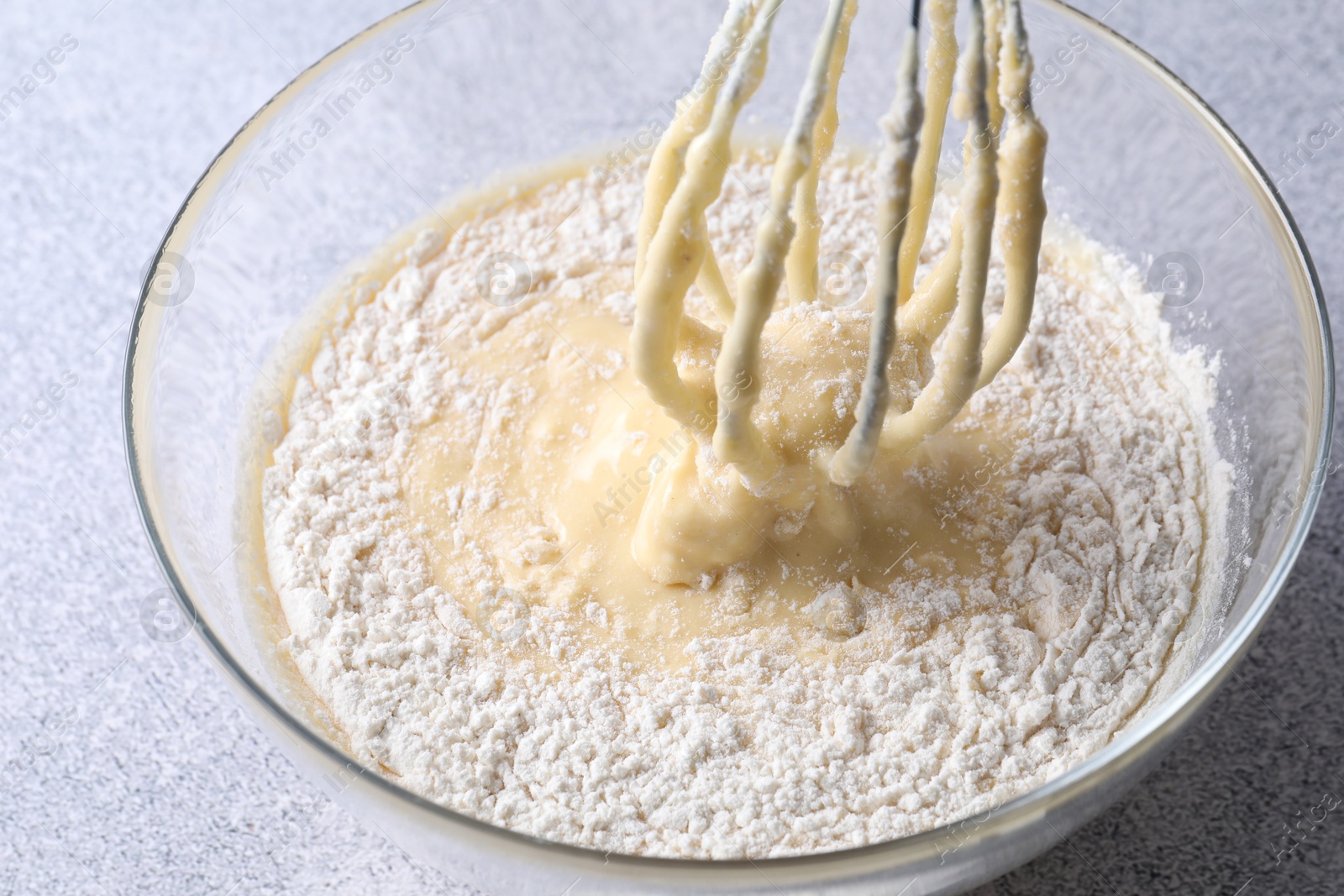 Photo of Whisk and bowl of dough on grey table, closeup