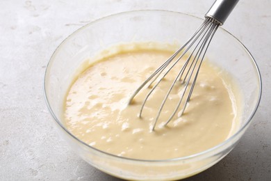 Photo of Whisk and bowl of dough on grey table, closeup