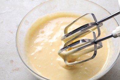 Photo of Making dough in bowl with hand mixer at grey table, closeup