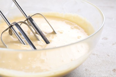 Photo of Making dough in bowl with hand mixer at grey table, closeup