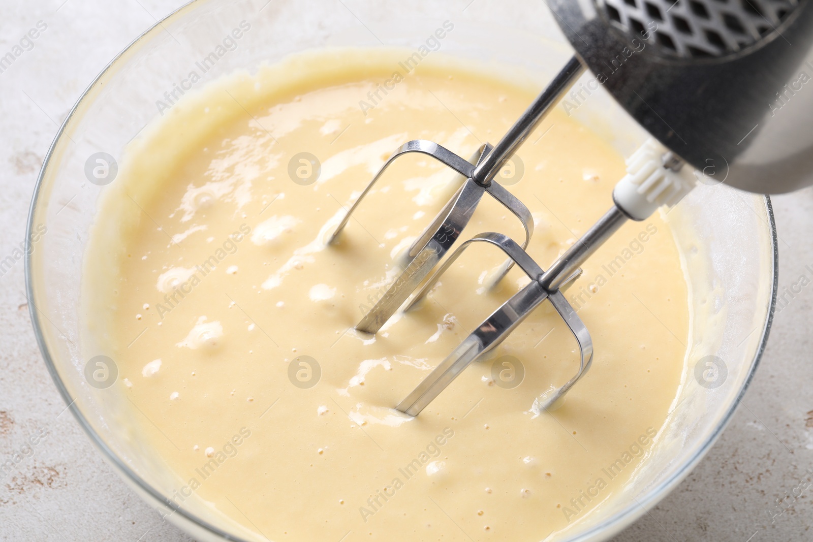 Photo of Making dough in bowl with hand mixer at grey table, above view