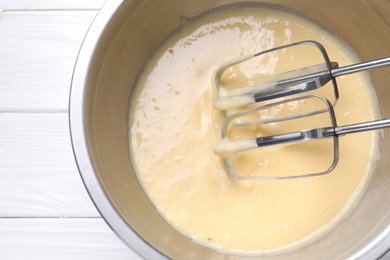 Photo of Making dough in bowl with hand mixer at white wooden table, top view