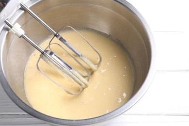 Photo of Making dough in bowl with hand mixer at white wooden table, closeup