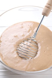 Photo of Whisk and bowl of dough on white table, closeup