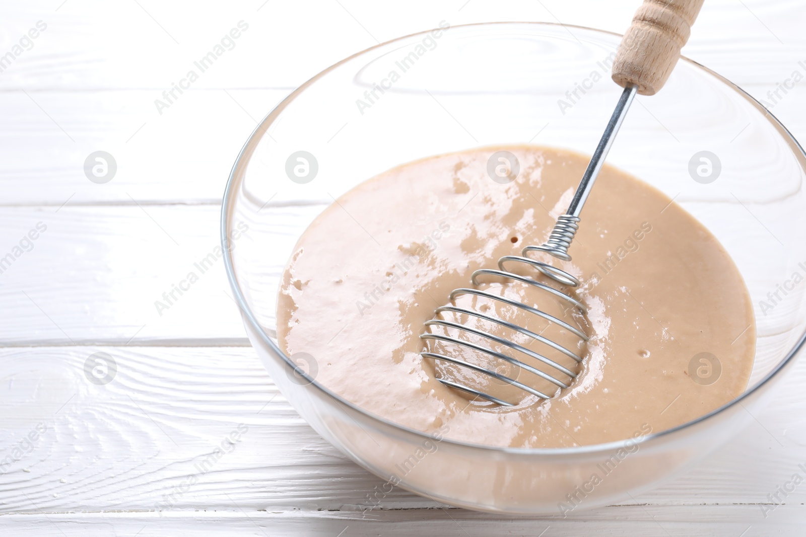 Photo of Whisk and bowl of dough on white wooden table, closeup. Space for text