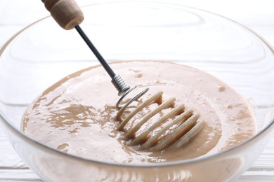 Photo of Whisk and bowl of dough on table, closeup