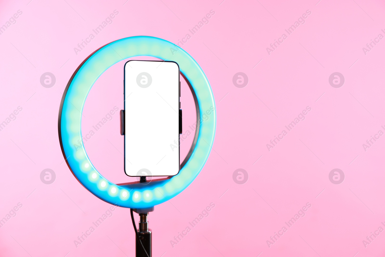 Photo of Ring lamp with smartphone on pink background, space for text