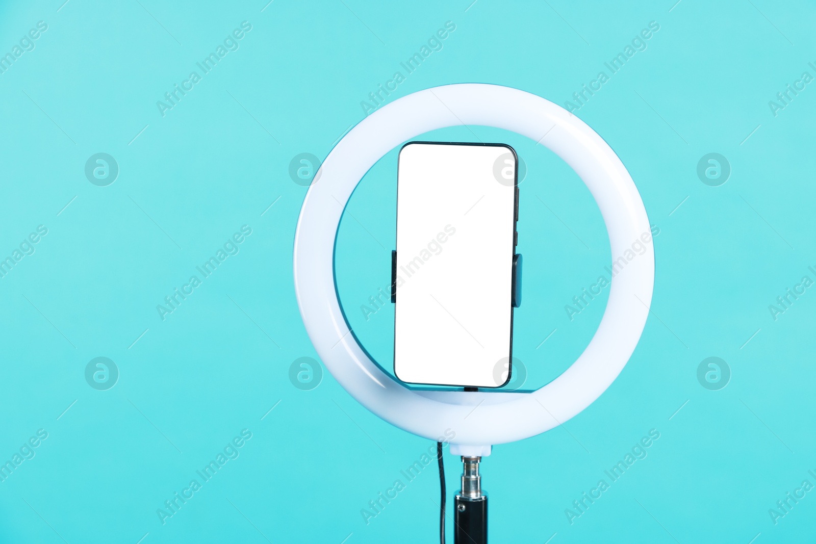 Photo of Ring lamp with smartphone on light blue background, space for text