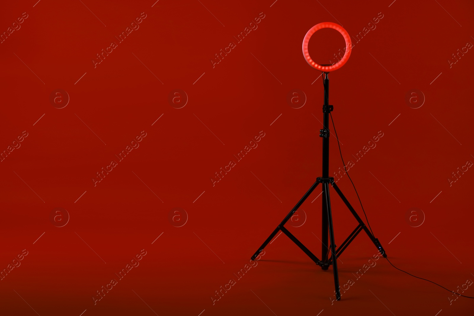 Photo of Ring lamp on stand against red background, space for text