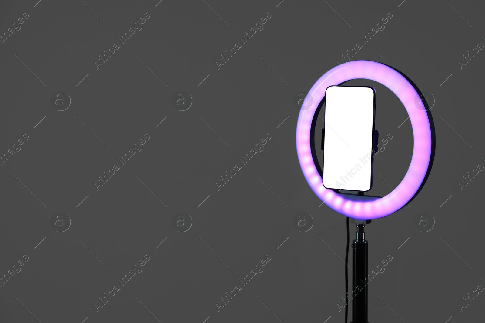 Photo of Ring lamp with smartphone on grey background, space for text