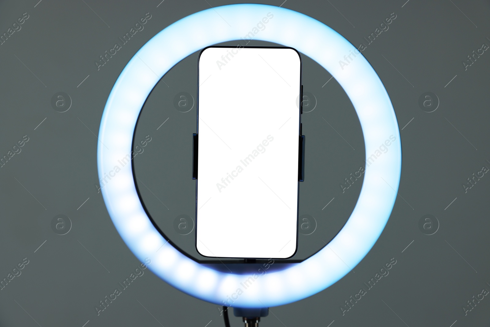 Photo of Ring lamp with smartphone on grey background, closeup