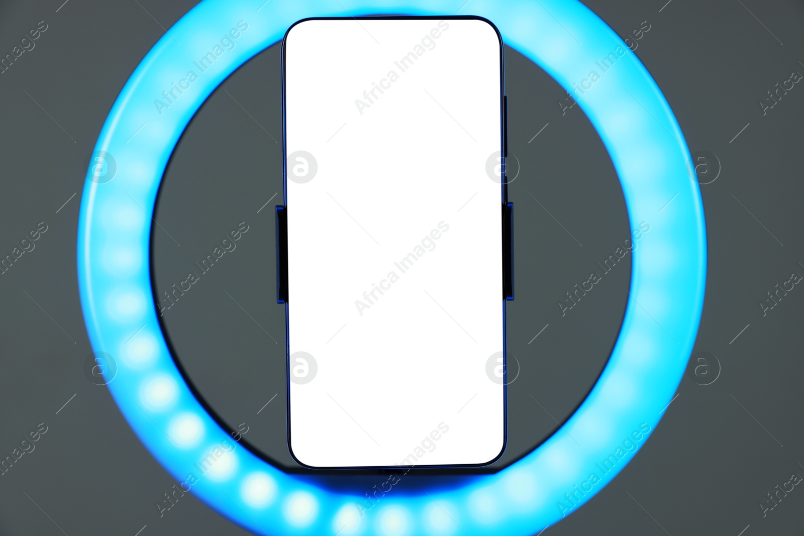 Photo of Ring lamp with smartphone on grey background, closeup