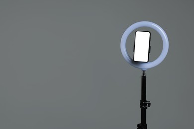 Photo of Ring lamp with smartphone on grey background, space for text