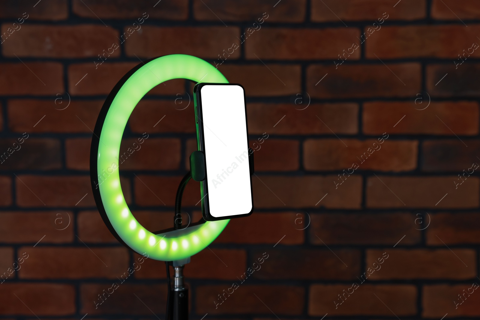 Photo of Ring lamp with smartphone against brick wall, closeup. Space for text