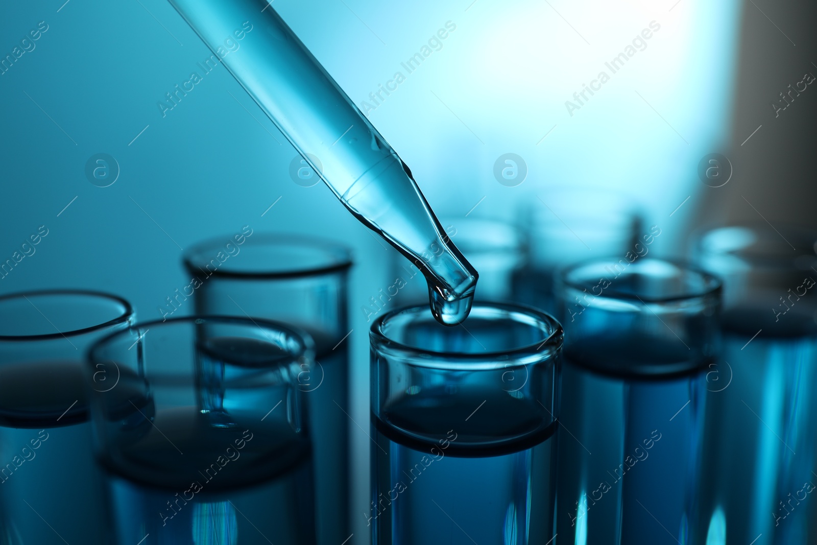 Photo of Dripping liquid into test tubes on blue background, closeup. Color toned effect