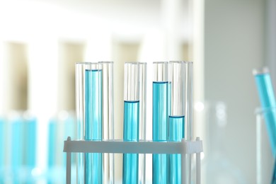 Photo of Test tubes with blue liquid in rack on blurred background, closeup