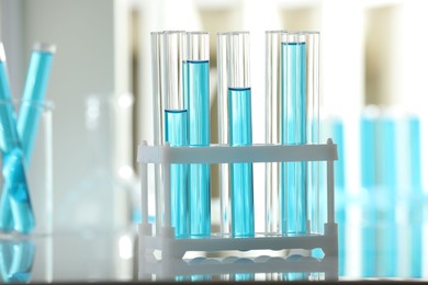 Photo of Test tubes with blue liquid in rack on blurred background, closeup