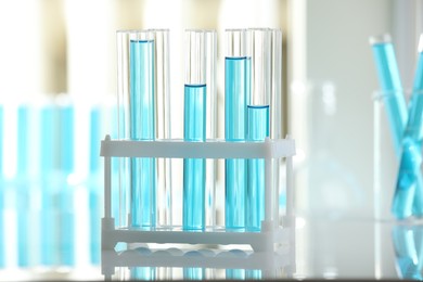 Photo of Test tubes with blue liquid in rack on blurred background, closeup