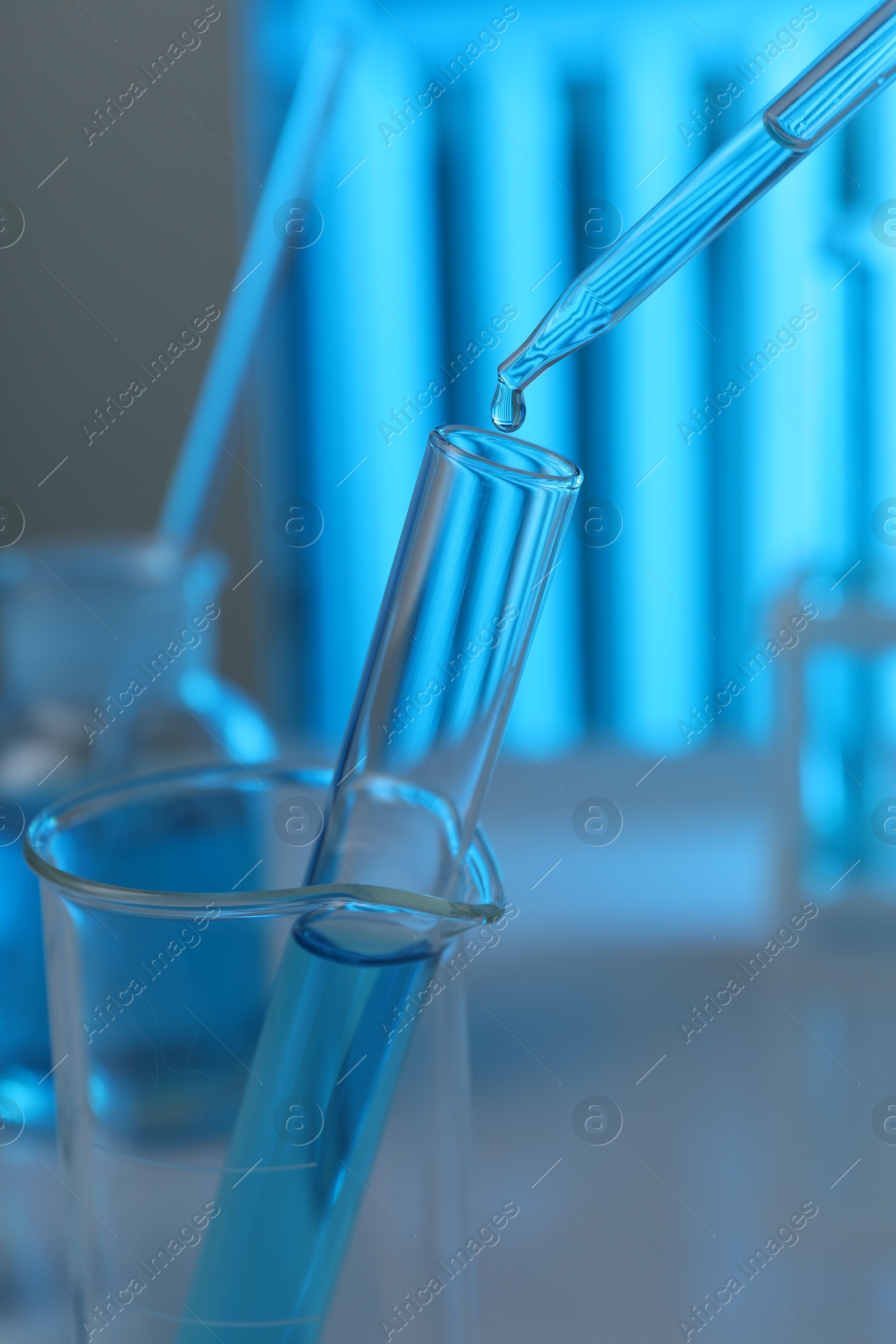 Photo of Dripping liquid into test tube on blurred background, closeup