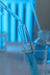 Photo of Dripping liquid into test tube on blurred background, closeup