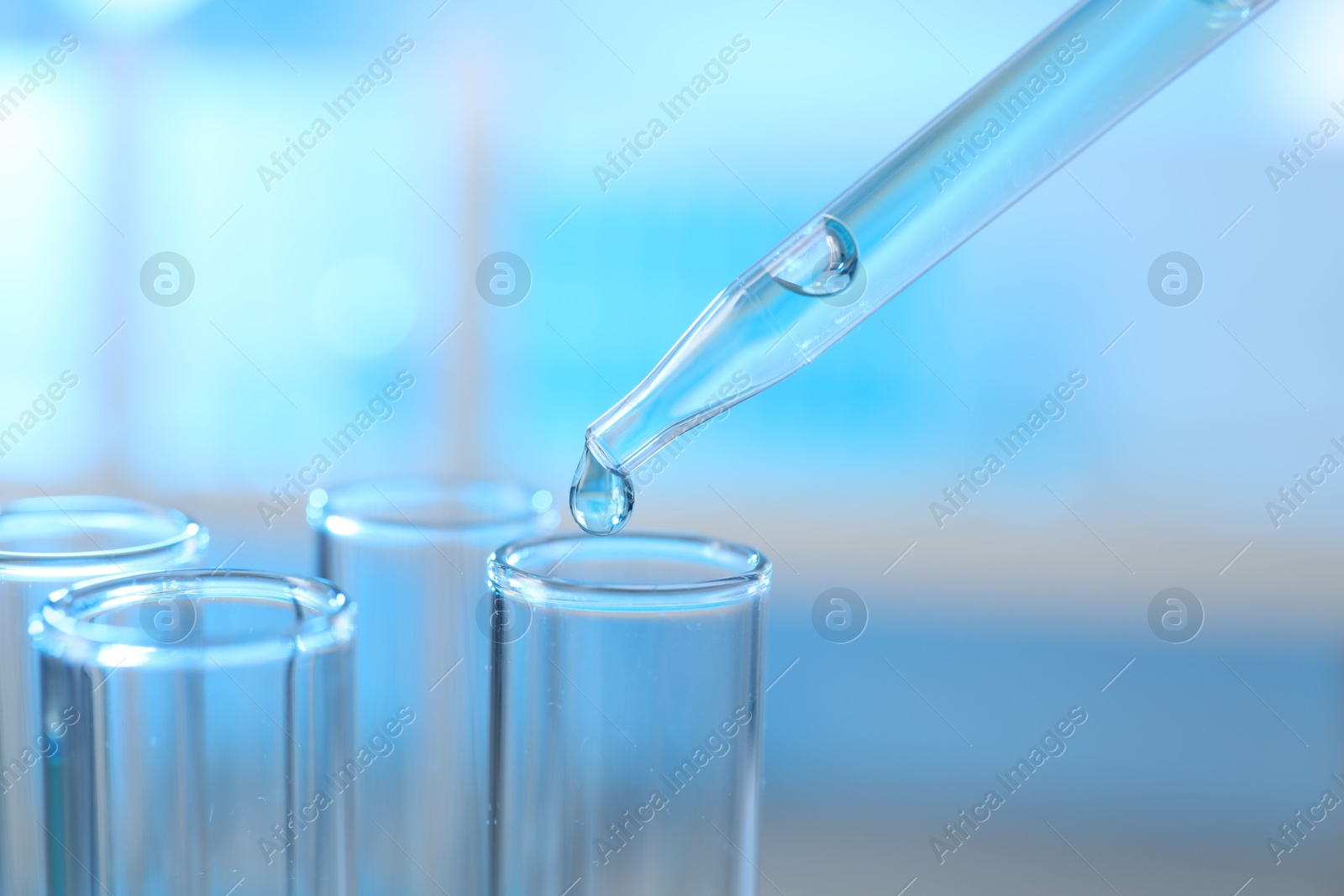 Photo of Dripping liquid into test tubes on light background, closeup